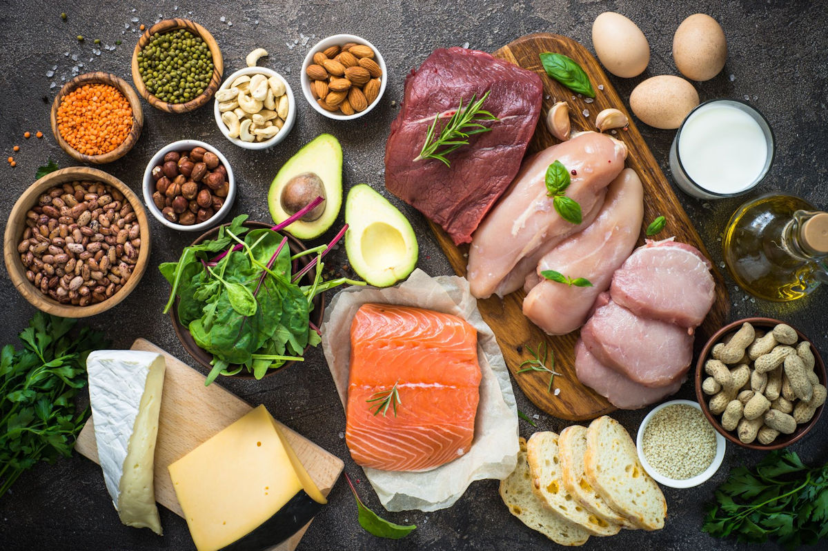 A selection of lean protein sources on a wooden table including salmon, beef, chicken, beans, eggs, legumes, and more.