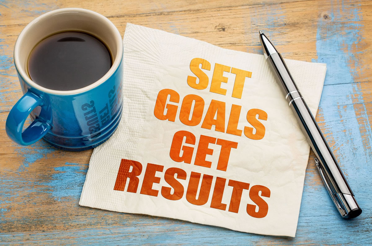 A coffee mug, pen, and a note that says "set goals, get results"