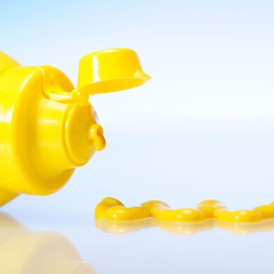A bottle of yellow mustard on its side with some mustard next to it.