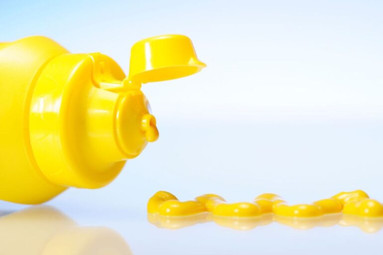 A bottle of yellow mustard on its side with some mustard next to it.
