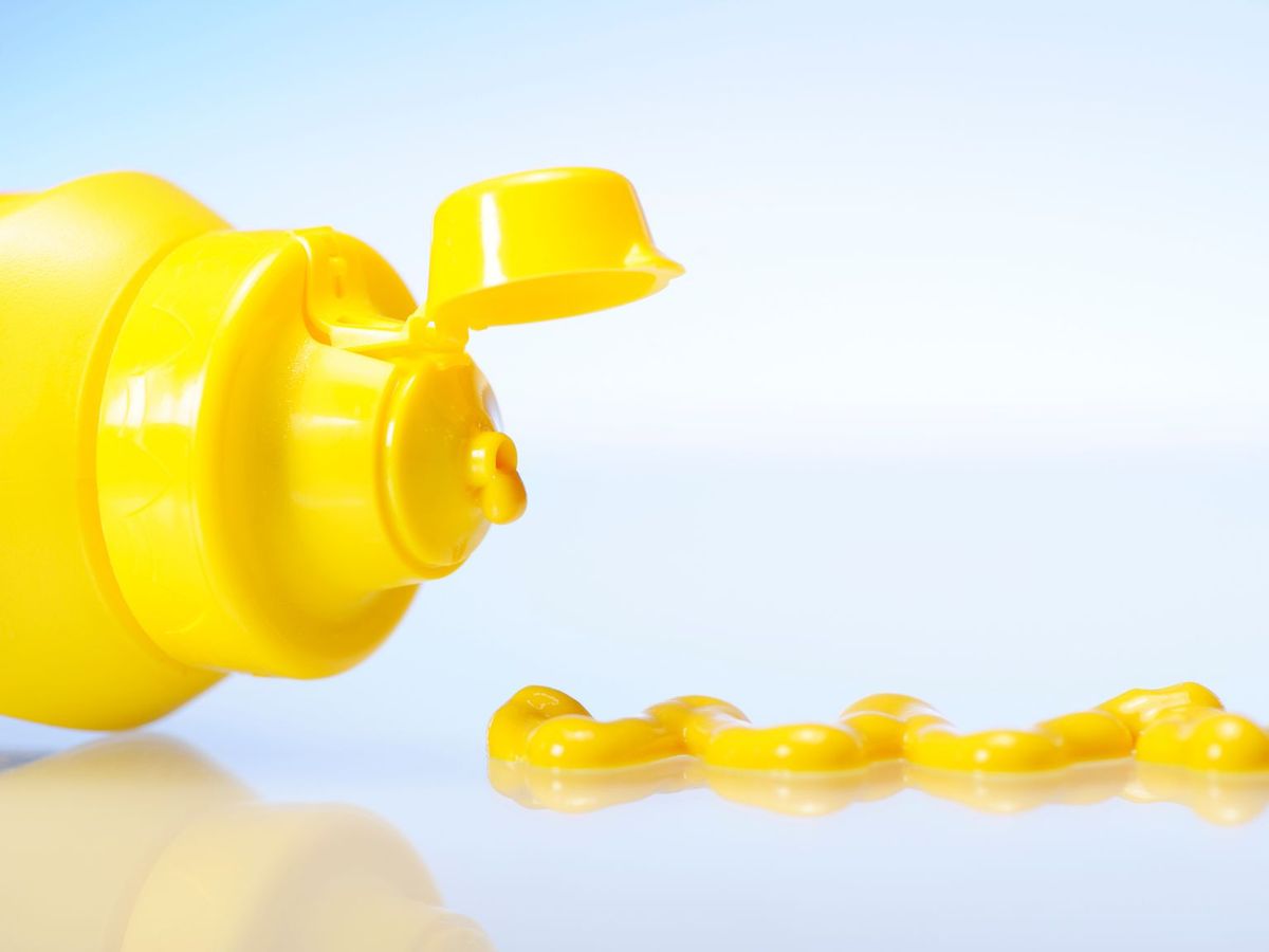 A bottle of yellow mustard on its side with some mustard next to it.