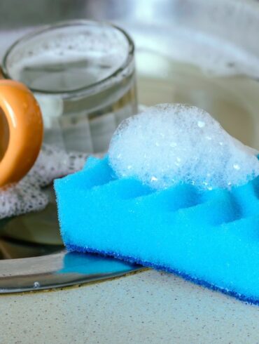 A dish sponge on the sink next to a pile of dirty dishes