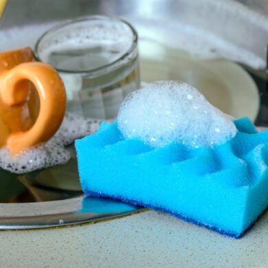 A dish sponge on the sink next to a pile of dirty dishes