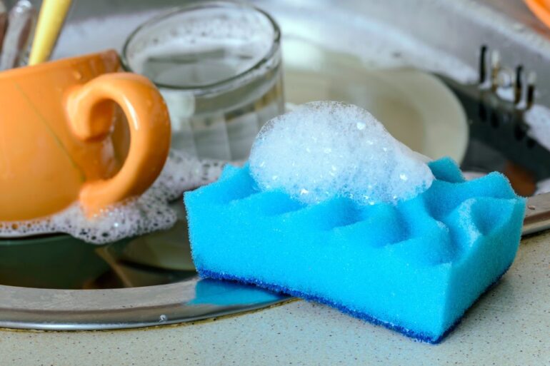 A dish sponge on the sink next to a pile of dirty dishes