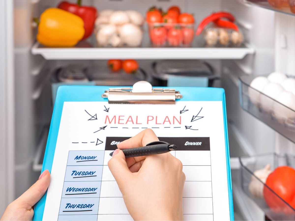 A person with a clipboard that says "meal plan" in front a fridge.