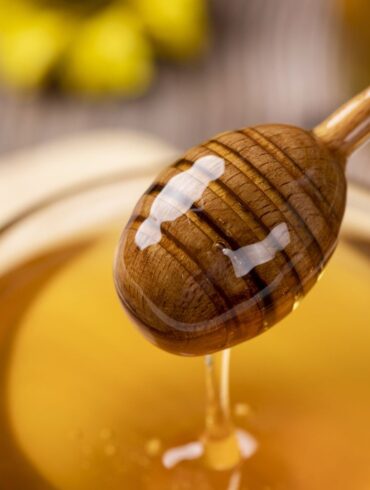A jar of honey and honey dipper with honey on it.