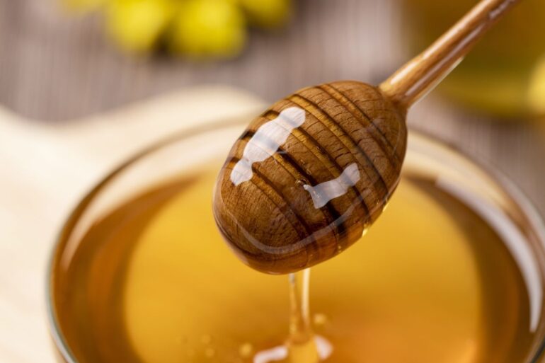 A jar of honey and honey dipper with honey on it.