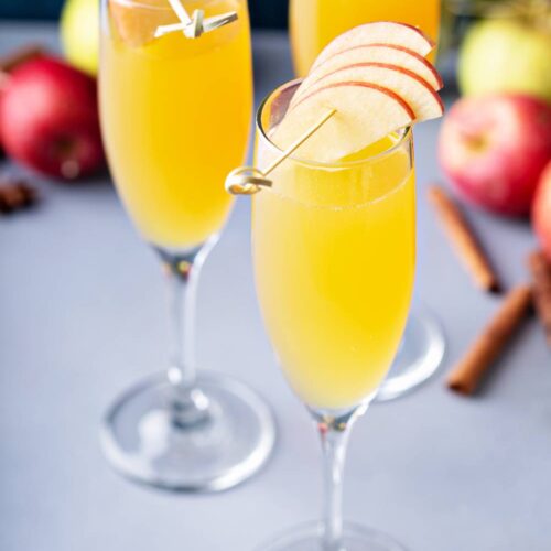 Three Apple Cider Mimosas in champagne glasses garnished with apples