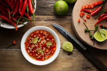 a bowl of fish sauce with peppers and limes on a cutting board with a knife.