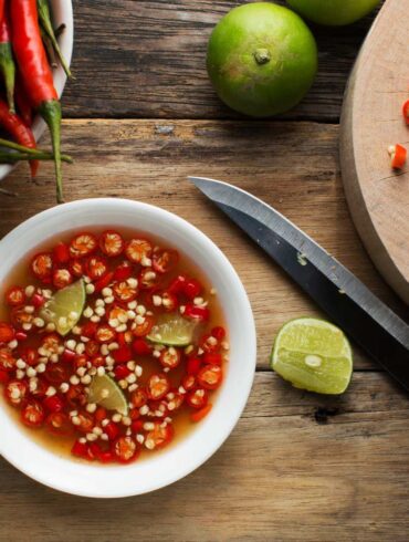 a bowl of fish sauce with peppers and limes on a cutting board with a knife.