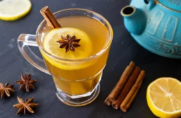A healthy hot toddy on a table with a tea pot, lemon, and star anise