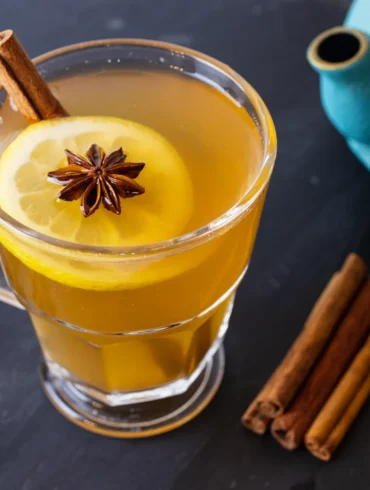 A healthy hot toddy on a table with a tea pot, lemon, and star anise
