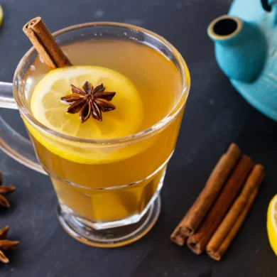 A healthy hot toddy on a table with a tea pot, lemon, and star anise