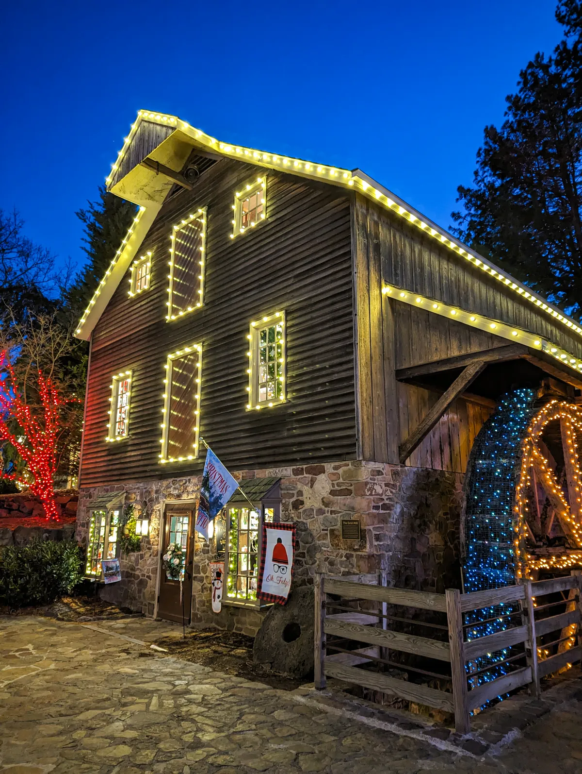 Pine Wreath & Candle shop decorated for the holidays at Peddler's Village with Christmas lights around the windows, roof, and waterwheel. 