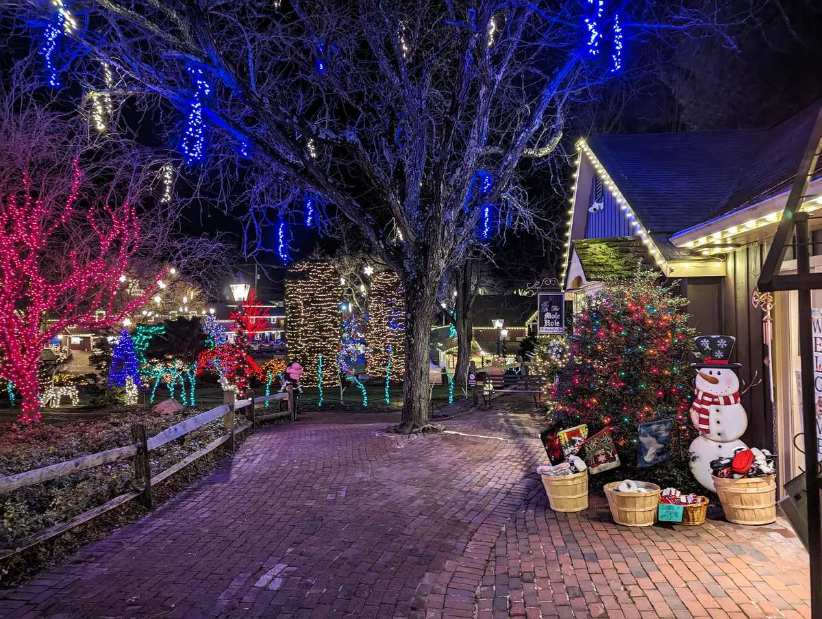 The holiday display outside of The Mole Hole Shop in Peddler's Village. Holiday lights are glowing down the path and there's a snowman outfront.