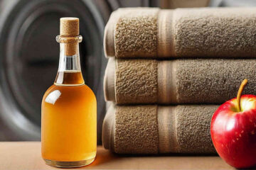 A bottle of apple cider vinegar next to an apple and folded, clean towels. A washing machine in the background.