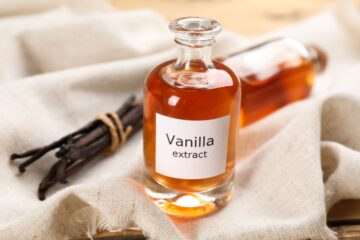 A bottle of vanilla extract next to vanilla beans on a table.