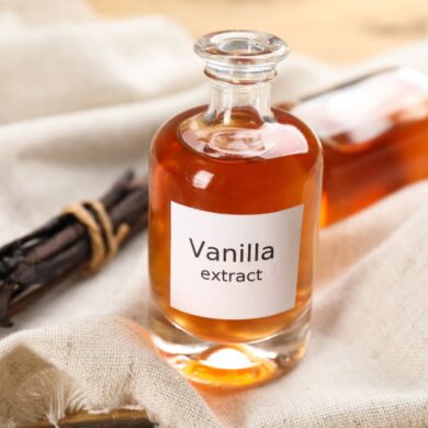 A bottle of vanilla extract next to vanilla beans on a table.