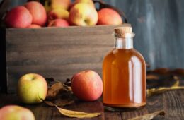 A bottle of apple cider vinegar next to a basket of apples