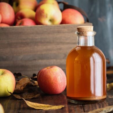 A bottle of apple cider vinegar next to a basket of apples