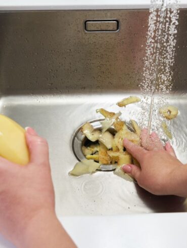 A person putting potato peels down the garbage disposal