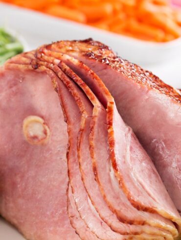 A full sliced, smoked ham on a food counter being prepped for the fridge.