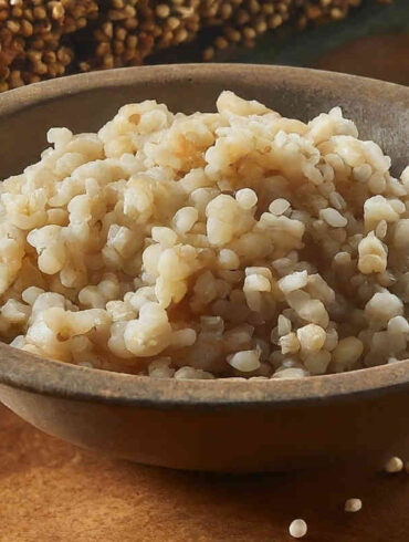 A rustic bowl of cooked sorghum on a table with uncooked sorghum and sorghum plants.
