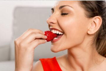 A woman eating a strawberry to support healthy teeth.