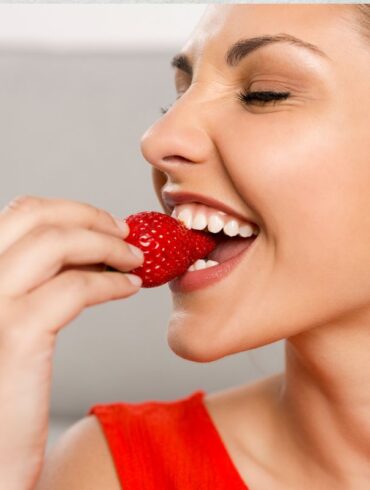 A woman eating a strawberry to support healthy teeth.