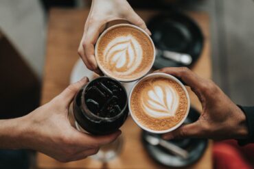 3 hands toasting 3 cups of coffee over a table.