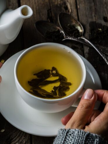a mug and pot of green tea on a rustic table.