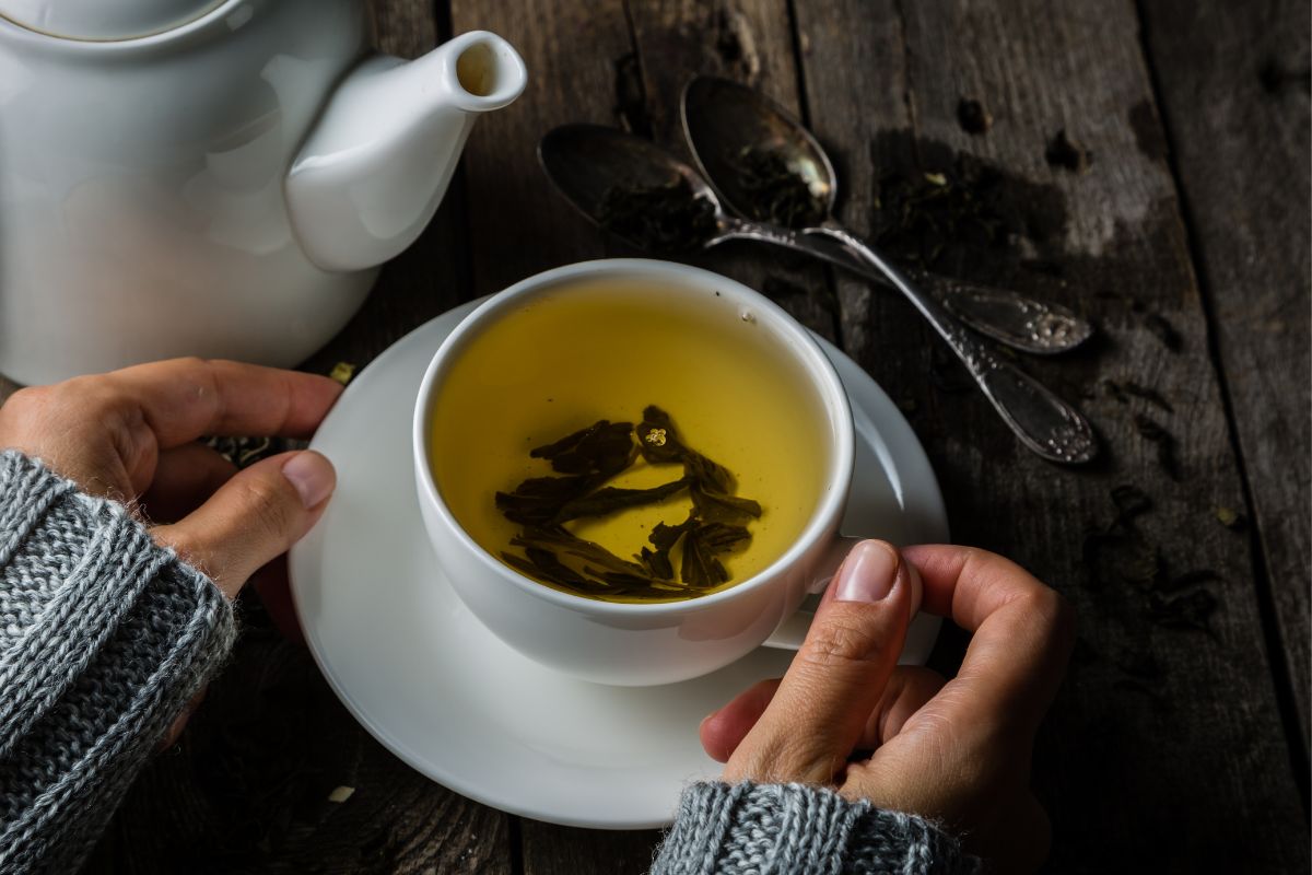 a mug and pot of green tea on a rustic table.