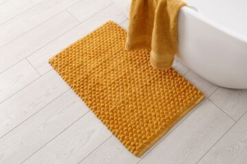 A bath mat on the floor next to a tub and towel, ready to be cleaned.