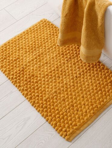 A bath mat on the floor next to a tub and towel, ready to be cleaned.
