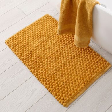 A bath mat on the floor next to a tub and towel, ready to be cleaned.