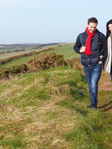 A man and woman walking a dog along a rolling hillside