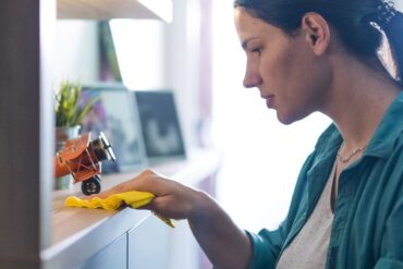 A woman with a dust rag cleaning a mantle.