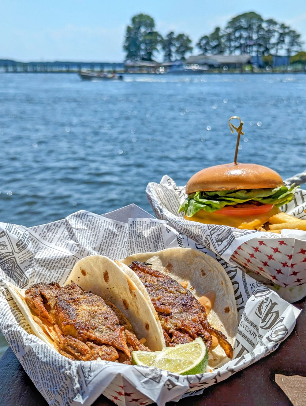 Two crab tacos and a burger with fries served on a table by the water at Big Owl Tiki Bar in Kent Narrows