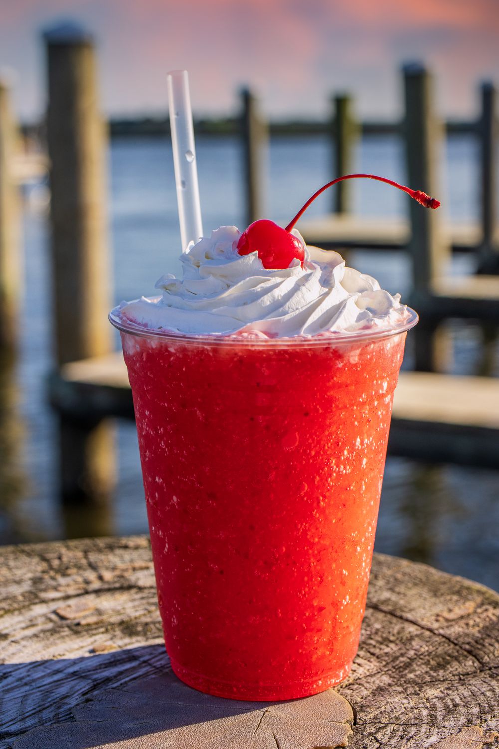 A bright red frozen drink topped with whipped cream and a cherry, with a scenic waterfront background at the Crab Deck in Kent Narrows.
