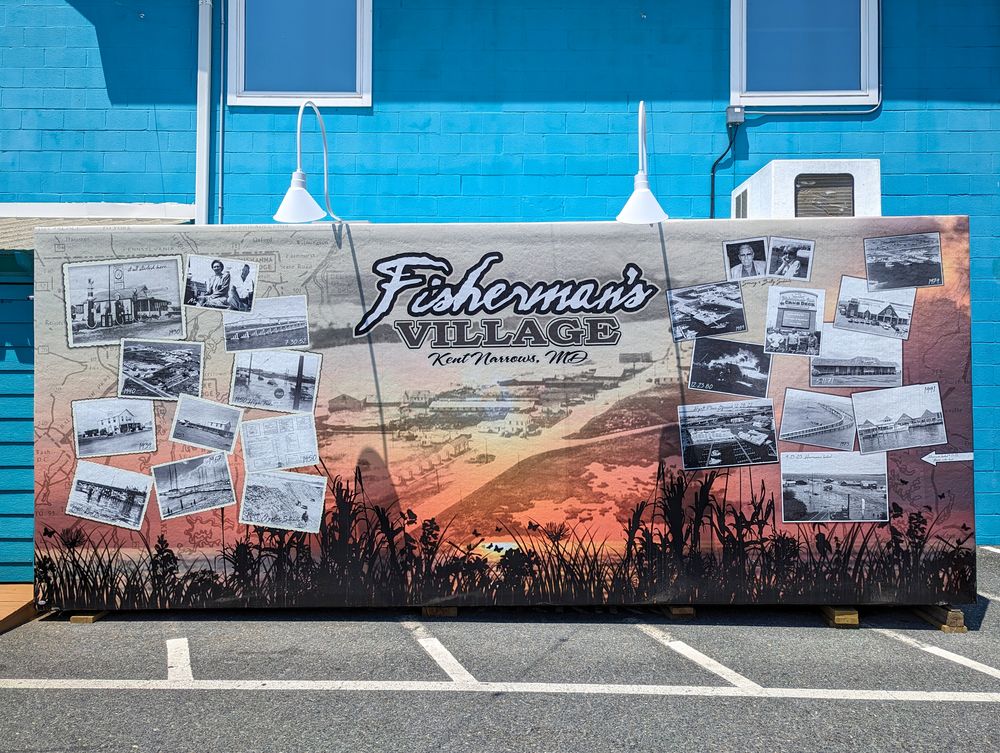 Large banner displaying 'Fisherman's Village' logo with vintage photographs of Kent Narrows, MD. The background shows a sunset beach scene with silhouetted grass. Multiple black and white photos showcase the area's historical buildings and landscapes.
