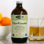 A bottle and mug of Flor-Essence herbal detox tea on a counter next to a bowl of citrus fruit.