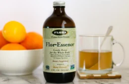 A bottle and mug of Flor-Essence herbal detox tea on a counter next to a bowl of citrus fruit.