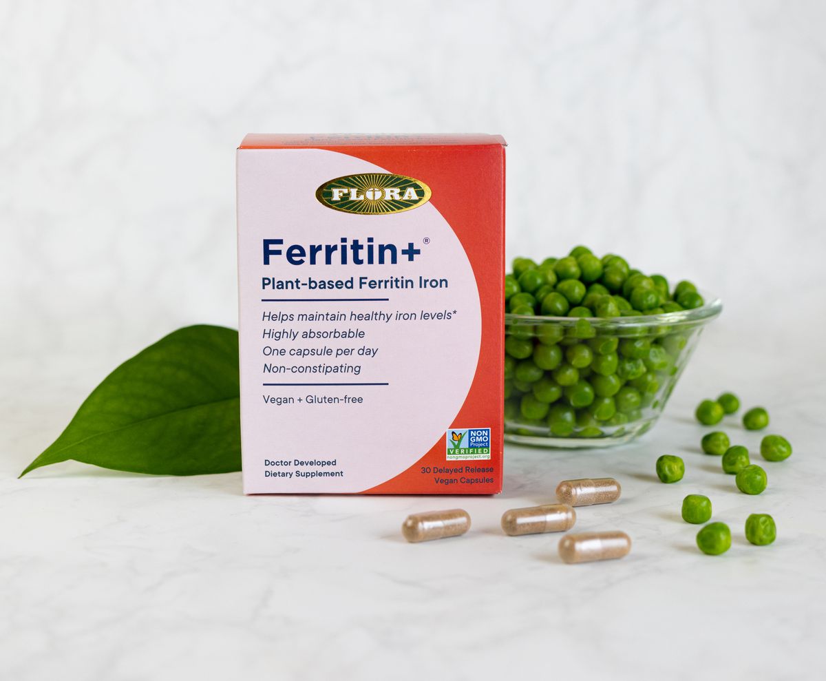 A box of Ferritin+ from Flora with a bowl of green peas and a leaf on a marble table. 