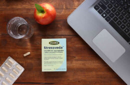 A box of Stressveda ksm-66 ashwagandha on a table with a laptop, water, and apple.