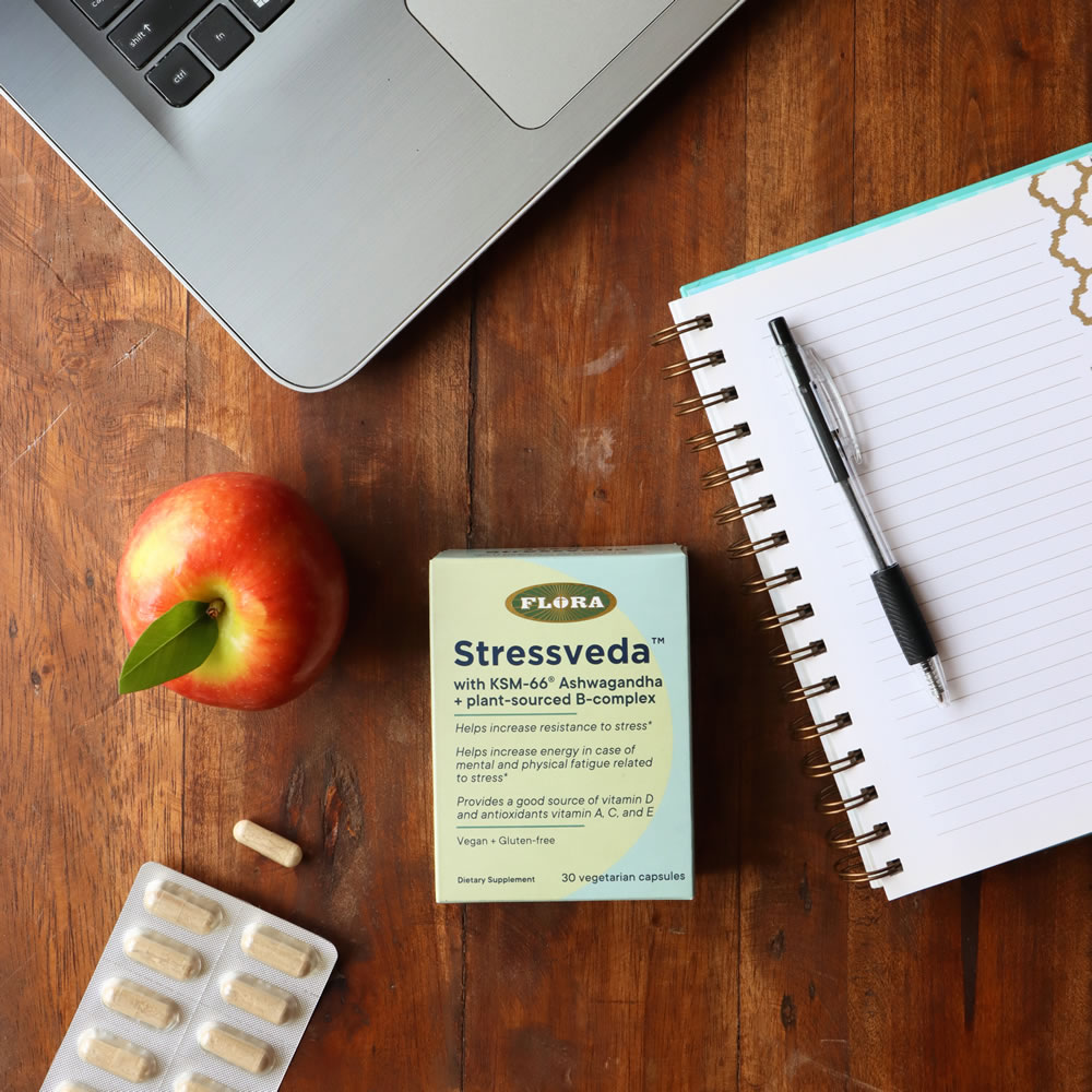 A box of Stressveda on a desk with a notepad, laptop, apple, and packaging. 