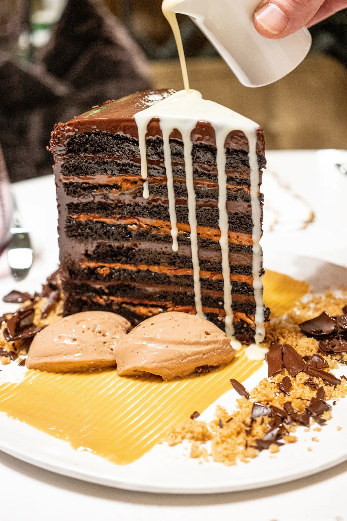 The Black Forest chocolate cake at Fawn & Fable. A towering piece of layered chocolate cake. Vanilla cream being poured atop. 