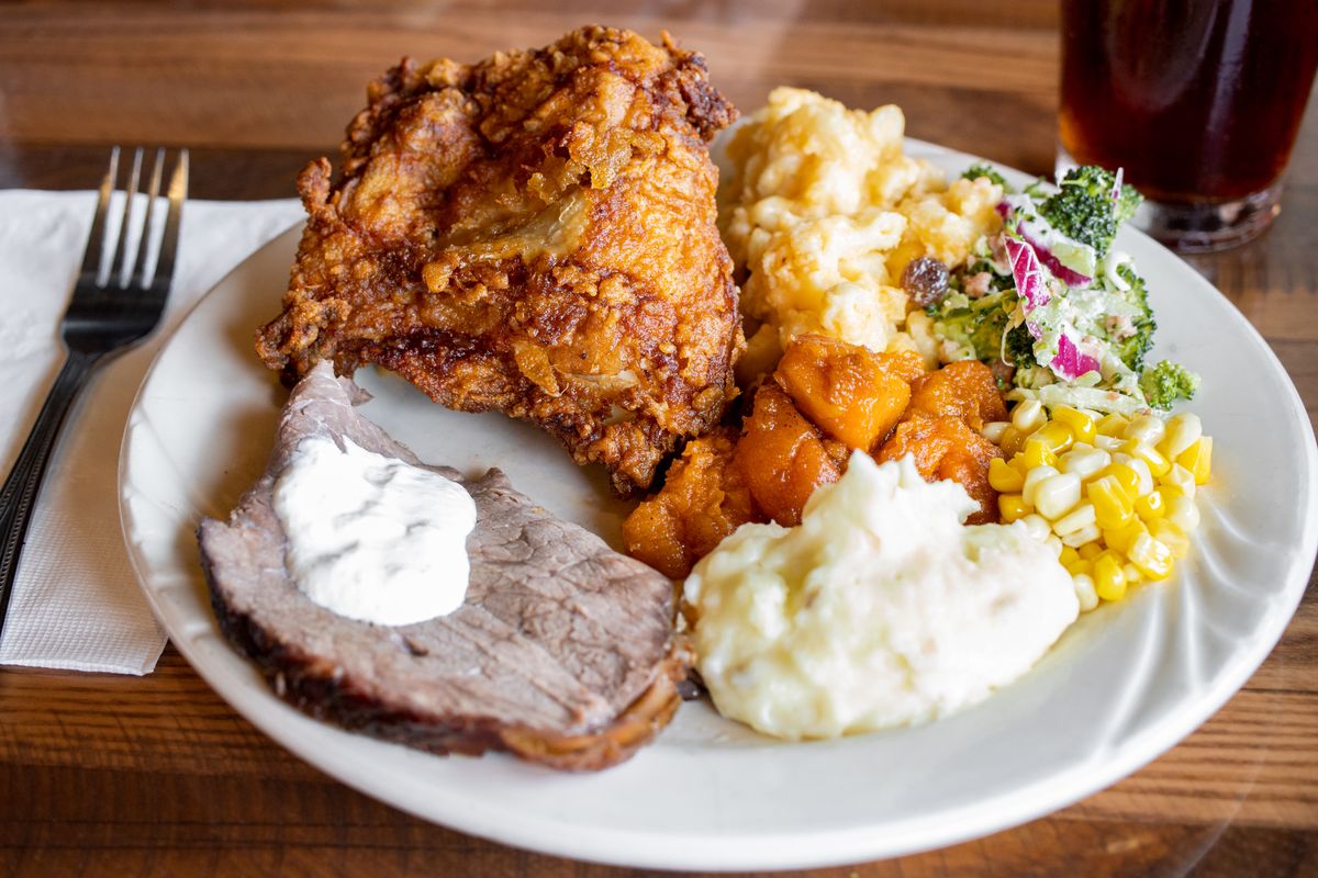 A plate loaded with various foods from Miller's, including fried chicken, roast beef with horseradish, mashed potatoes, corn, candied yams, and salad. 
