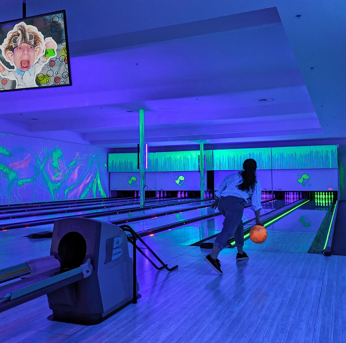 Cosmic Bowling at The Peak. A women bowling with a florescent ball under the blacklight and vibrantly painted alley. 