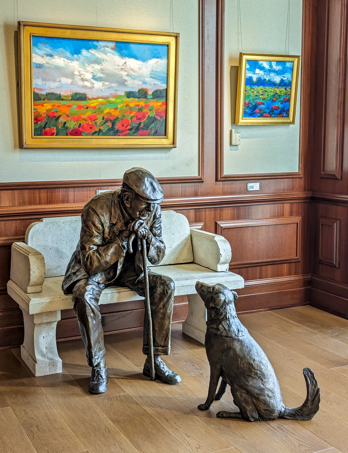 The Hardy Family Art Collection on display at Nemacolin. 2 painting and a sculpture of a man and dog. 