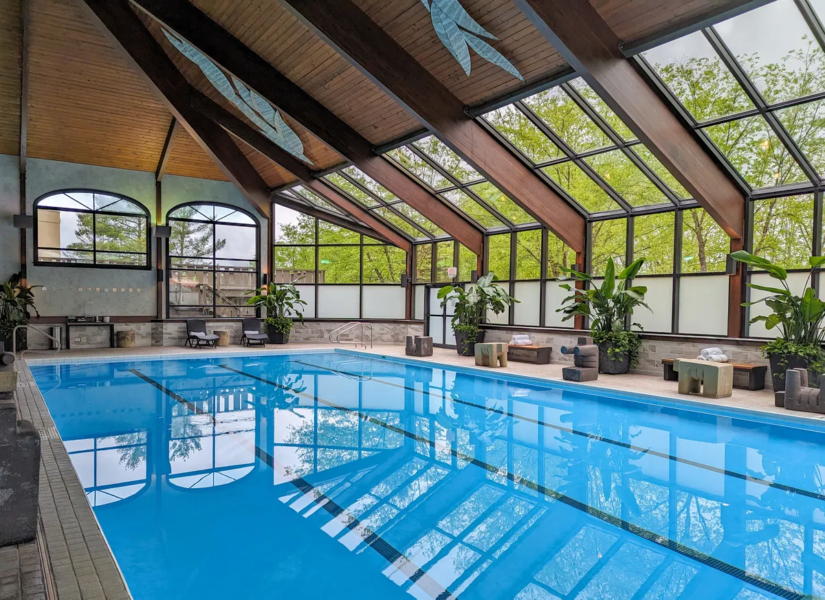 The four-lane indoor lap pool — heated to 84 degrees year-round at Woodlands Spa. An expansive pool room with plants and lounge chairs. 